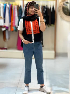 مدل زنانه با جلیقه سوزن دوزی مشکی نارنجی و شلوار جین در بوتیک