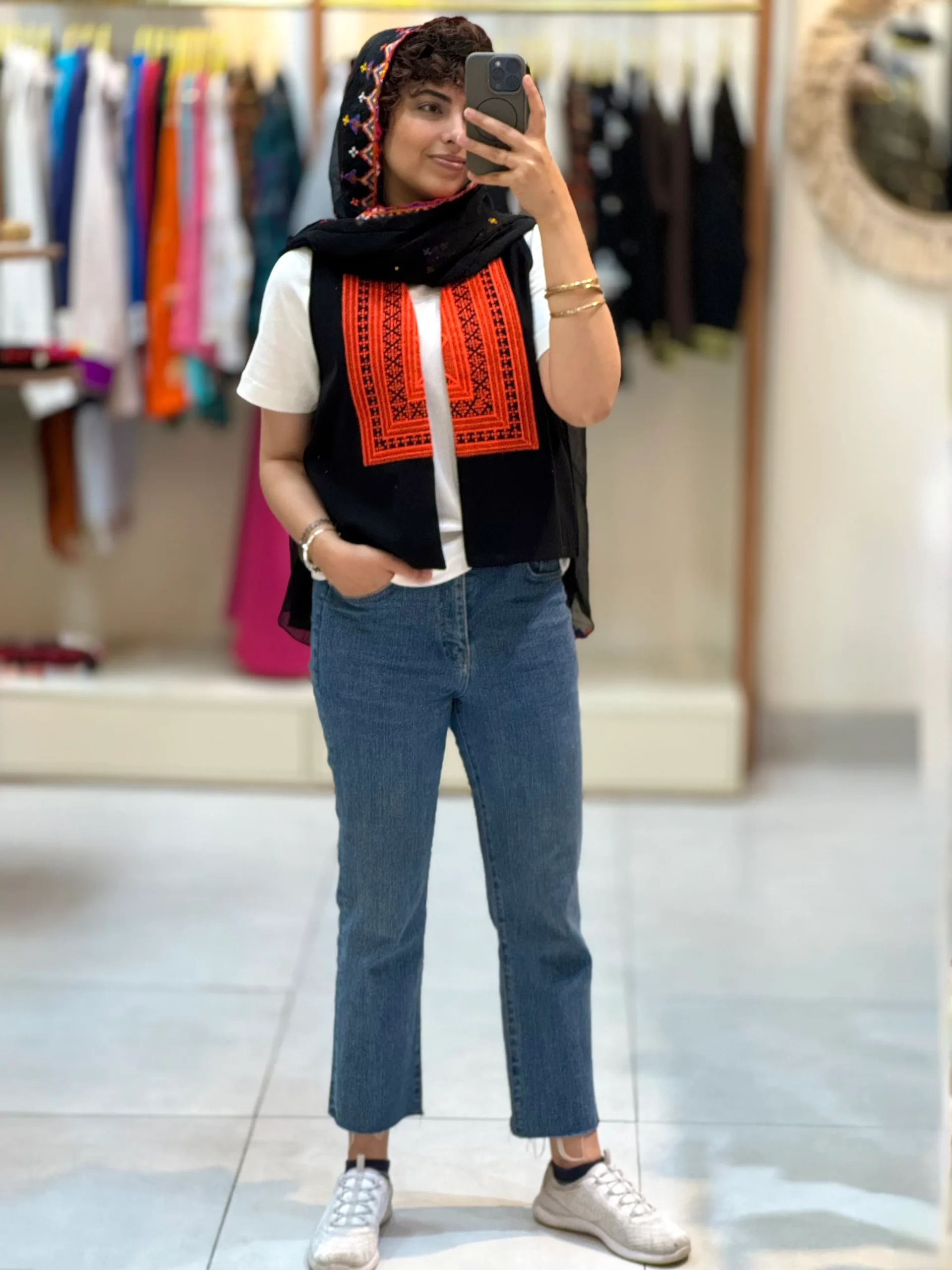مدل زنانه با جلیقه سوزن دوزی مشکی نارنجی و شلوار جین در بوتیک